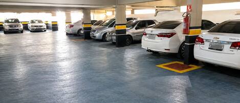 A parking garage with multiple rows of parked cars, fire extinguishers, and a fire hose on the right.