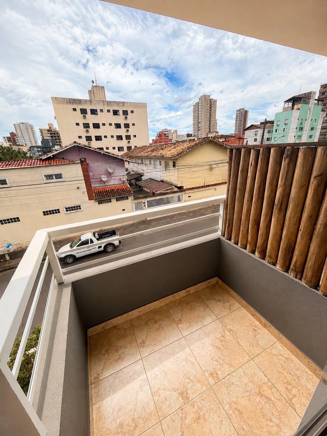 Ein Balkon mit Blick auf eine Stadtlandschaft, ein weißes Fahrzeug auf der Straße und ein Holzzaun.