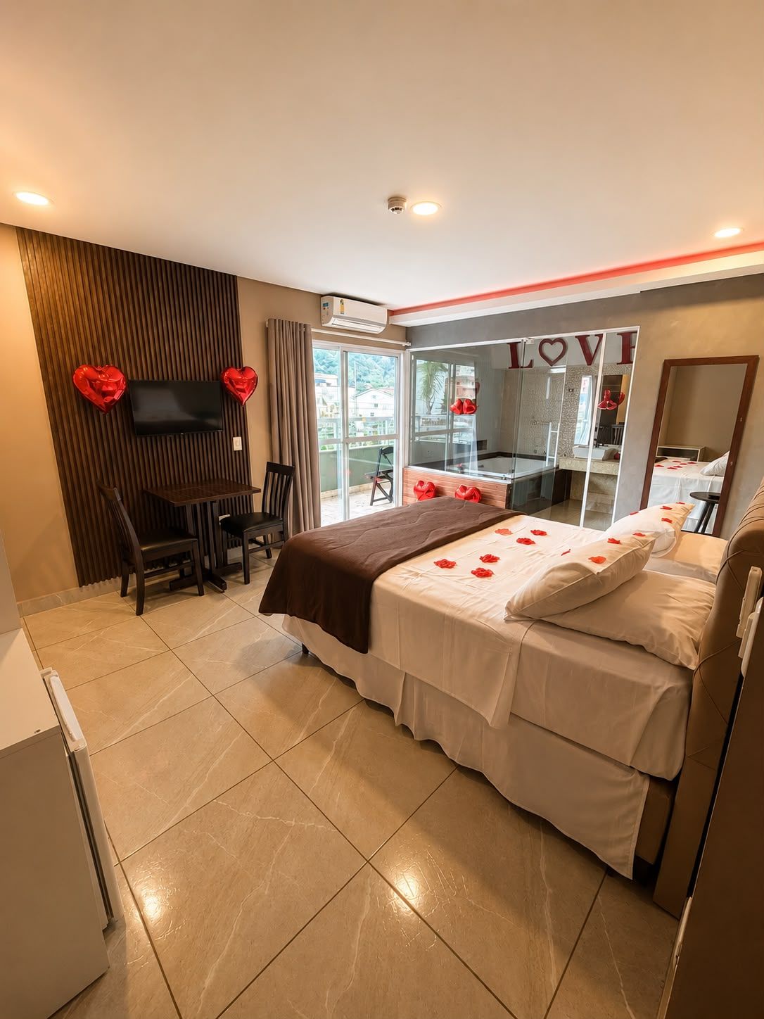 Une chambre d’hôtel avec un lit, un téléviseur fixé au mur, un bureau avec des chaises et une grande fenêtre.