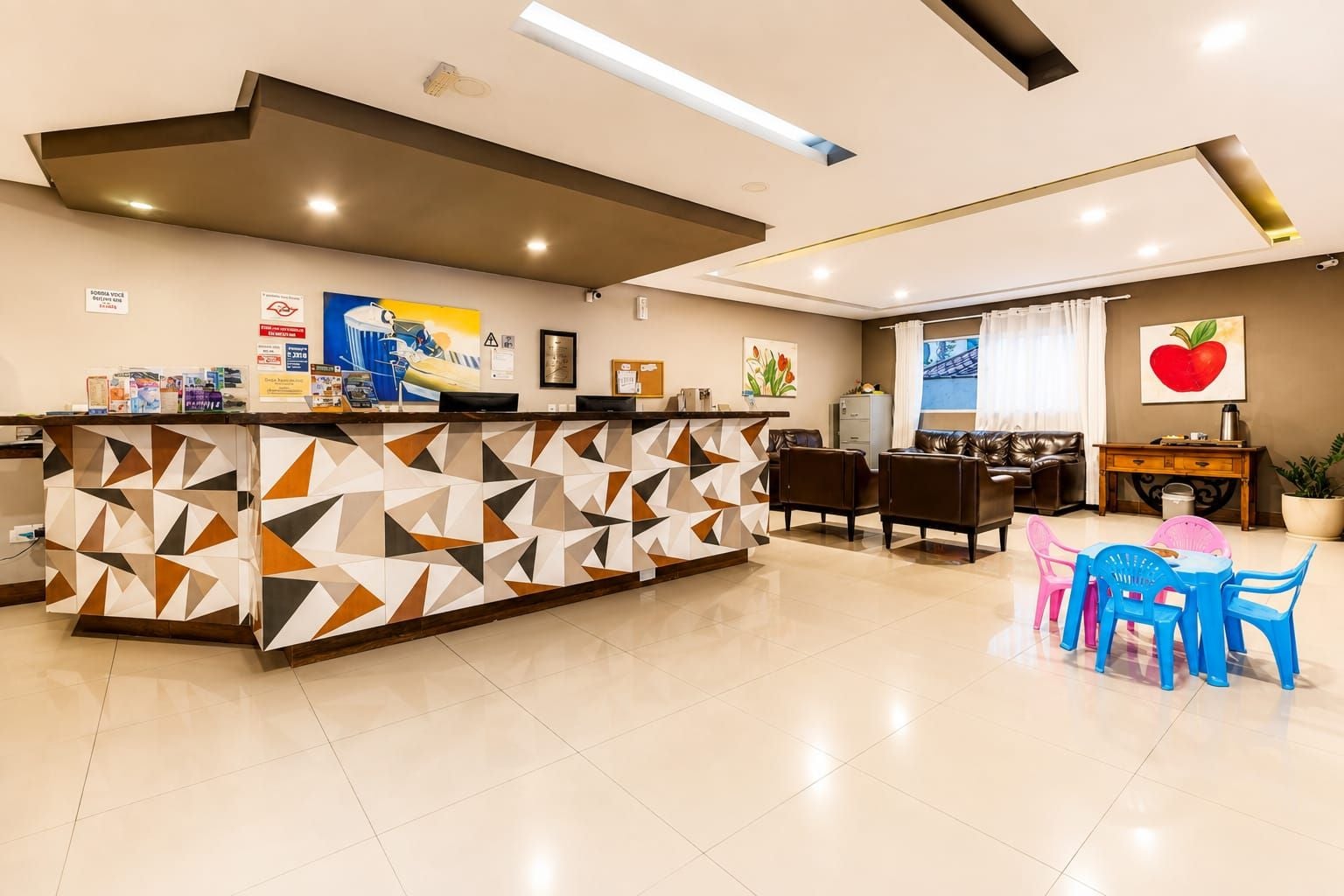 A reception area with a geometric-patterned counter, a dining area with a table and chairs, and a living room with a sofa and a large potted plant.