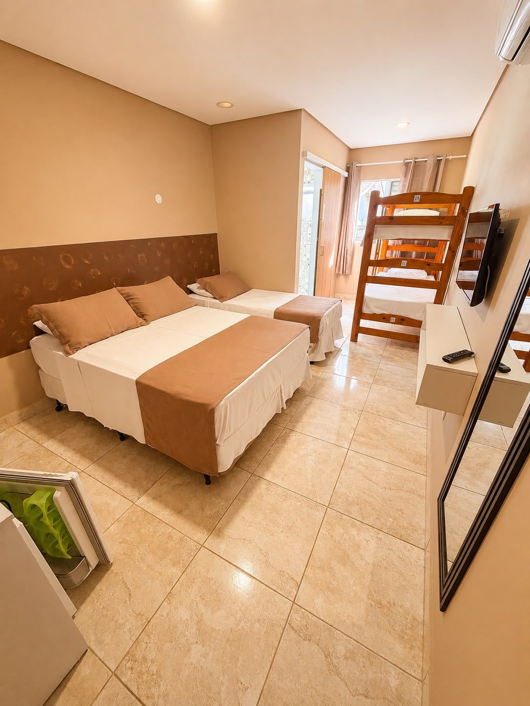 A hotel room with two beds, a desk, a chair, a TV, and a bathroom with a shower.