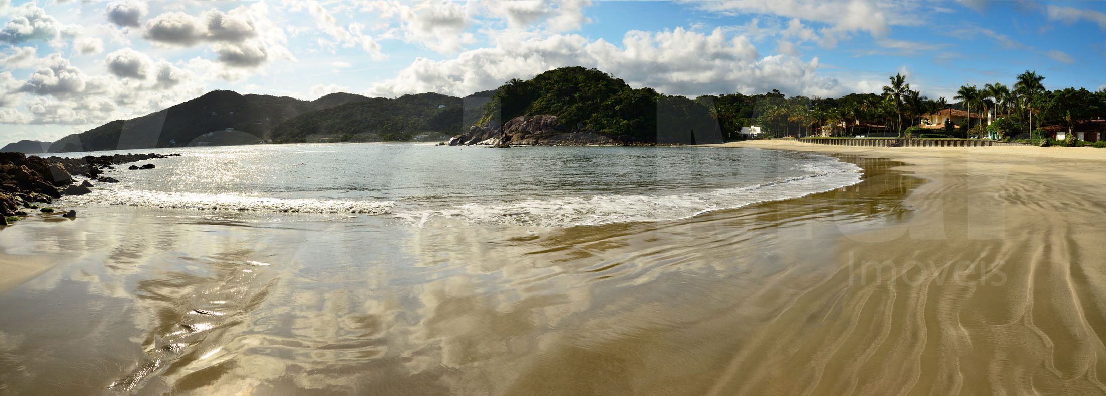 Una playa con agua cristalina, una orilla arenosa y una colina boscosa al fondo.