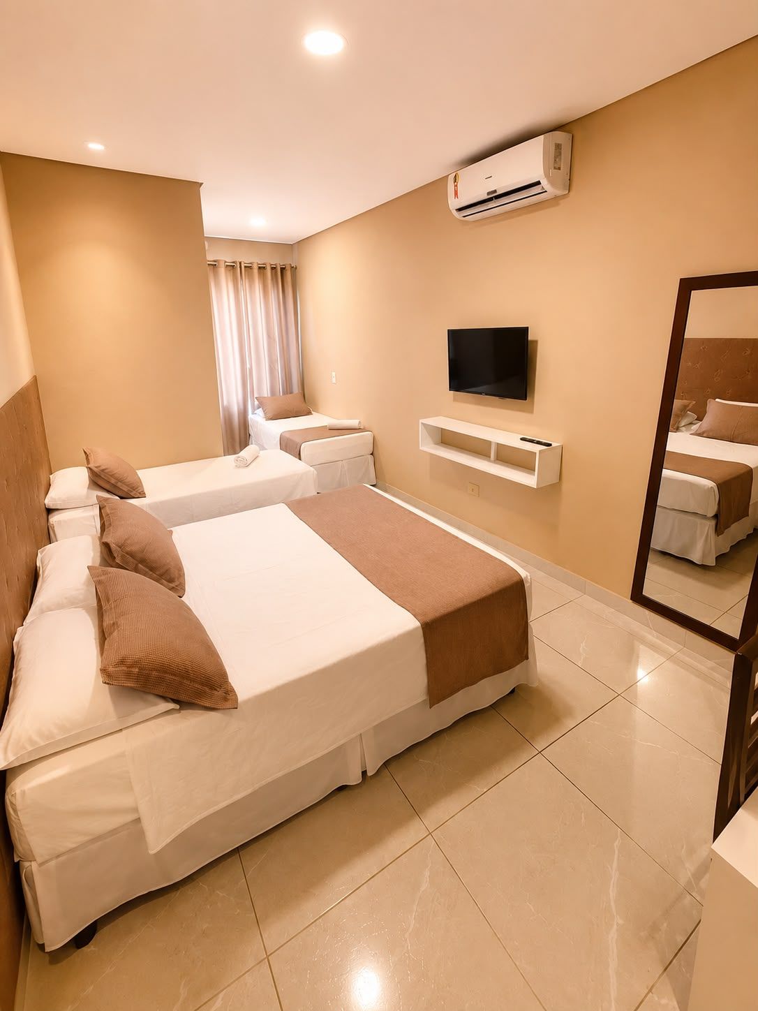 Habitación de hotel con una cama grande, un televisor, un aire acondicionado y un espejo.