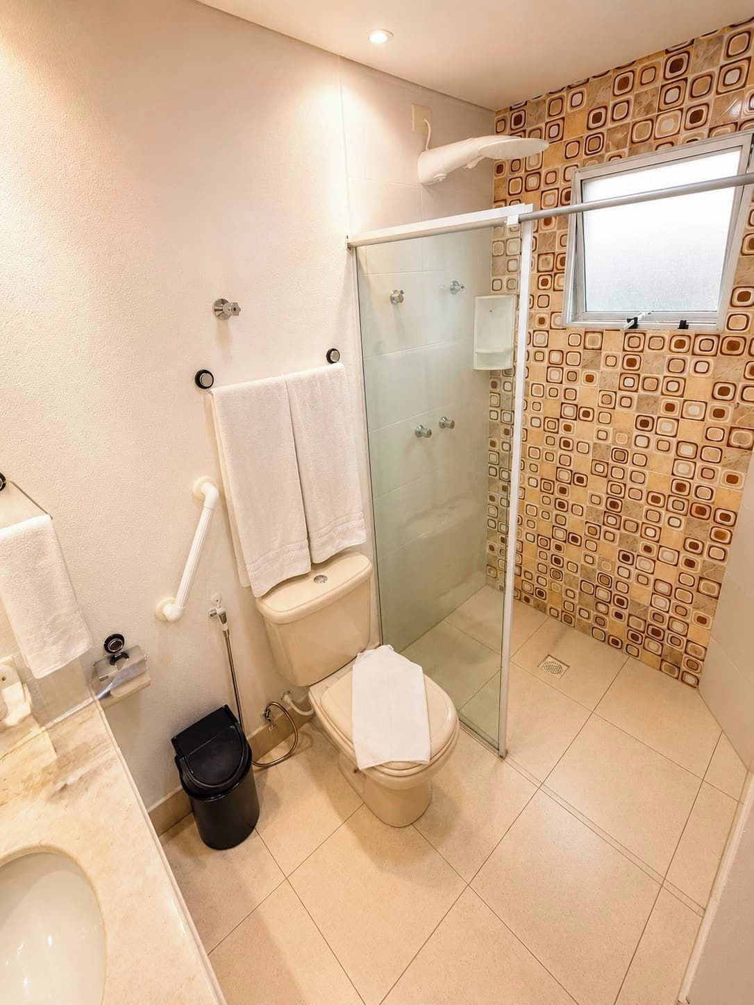 Un baño con inodoro, cabina de ducha de vidrio, lavabo y cubo de basura negro.
