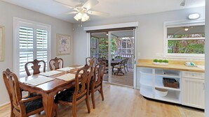 A dining area with a wooden table and chairs, a ceiling fan, and a sliding glass door leading to an outdoor patio. - Tropical Anna Maria Island Villa (Holmes Beach)