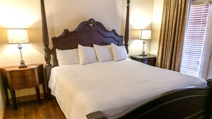 Een net opgemaakt bed met een houten hoofdbord, twee nachtkastjes met lampen en een raam met gordijnen.