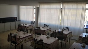 A dining area with tables covered in checkered tablecloths, chairs, and a kitchen area with cabinets and a black countertop. - Hotel Lisboa (Curitiba)