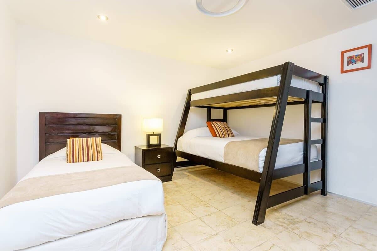 A bedroom with a bunk bed, a single bed, a nightstand with a lamp, and a picture on the wall.