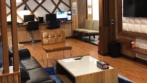 A modern lounge area with a wooden ceiling, a large flat-screen TV, leather seating, and a reception desk with computers. - Millennium Island Residence (Fuvahmulah)
