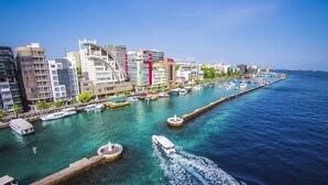 A waterfront cityscape with modern buildings, a marina with boats, and a clear blue sky. - Millennium Island Residence (Fuvahmulah)