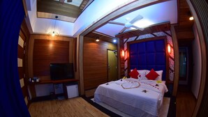 A bedroom with a large bed, a TV, wooden paneling, and a ceiling fan. - Millennium Island Residence (Fuvahmulah)