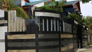 A modern house with a black and beige exterior wall, a gated entrance, and a small garden area. - Millennium Island Residence (Fuvahmulah)