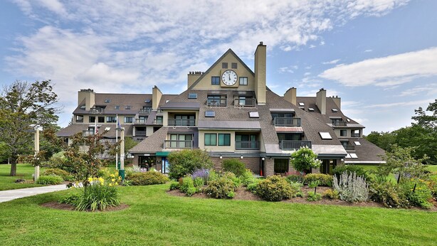 A multi-story building with a clock on the facade, surrounded by well-maintained lawns and various plants. - Charming, Renovated 2BR/2BA Mt Green Condo: Steps to Killington 3C13/A (Killington)