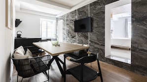 A modern dining area with a wooden table, black chairs, a TV mounted on a marble wall, and a view of a bathroom through an open doorway. - Via del Tritone (Rome)