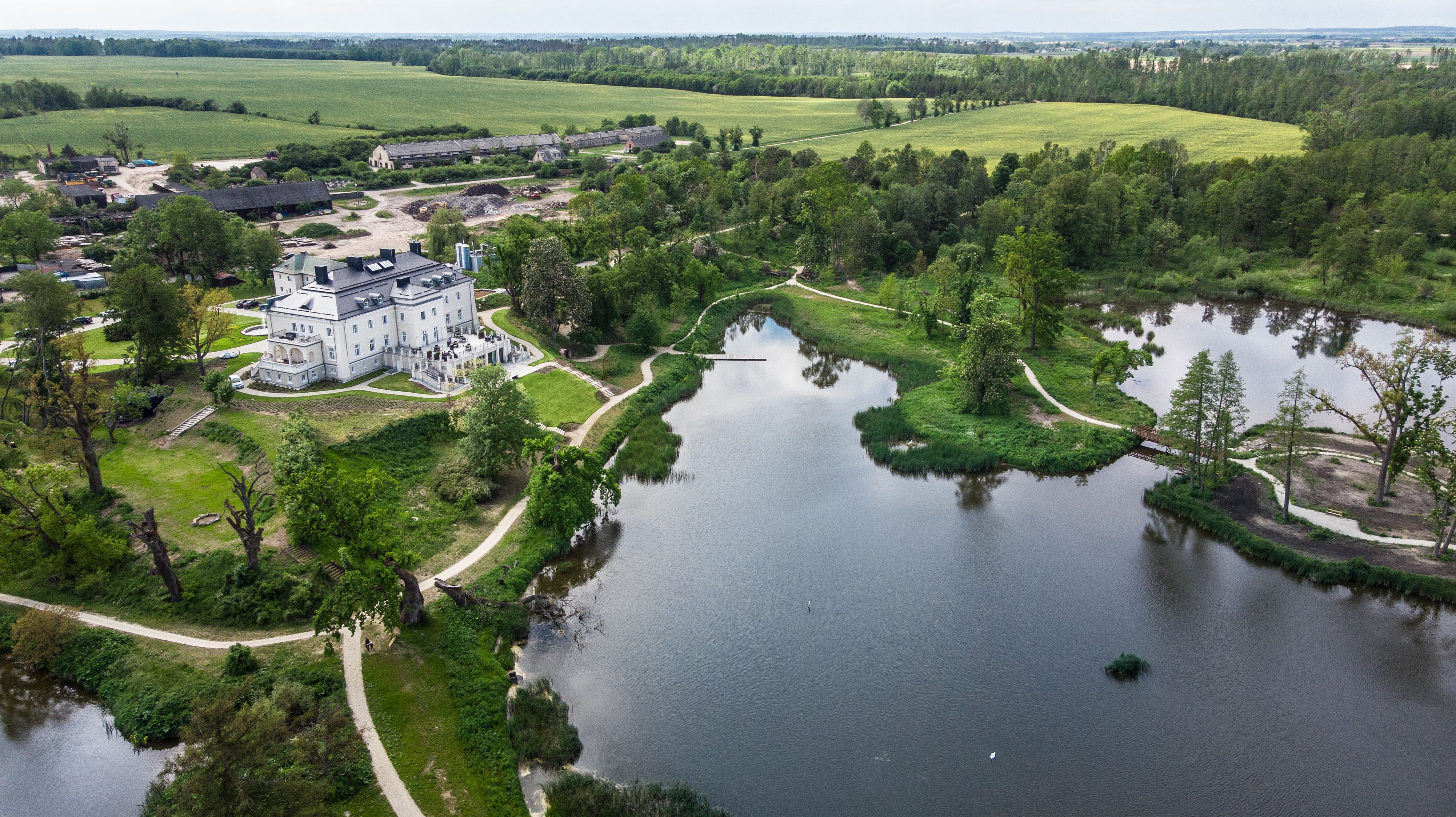Una extensa propiedad con un lago central, rodeada de exuberante vegetación y un edificio imponente de varias secciones.