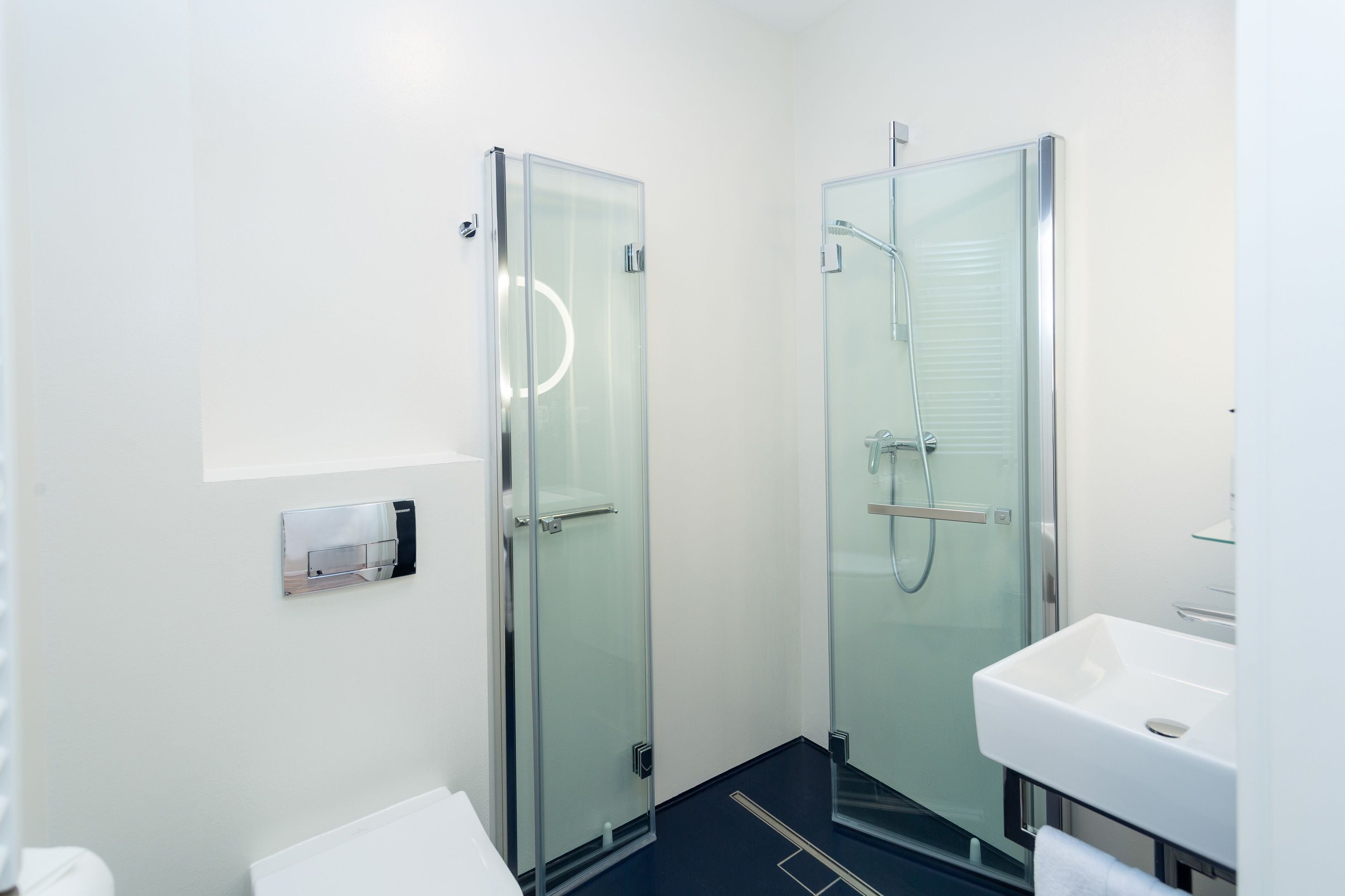 Een moderne badkamer met twee douchecabines van glas, een witte wastafel en een handdoekrek.