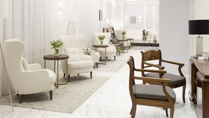 Un salón moderno con un sofá blanco, una silla de madera y una mesa de centro. Hay un cuadro en la pared y una lámpara sobre una mesita auxiliar.