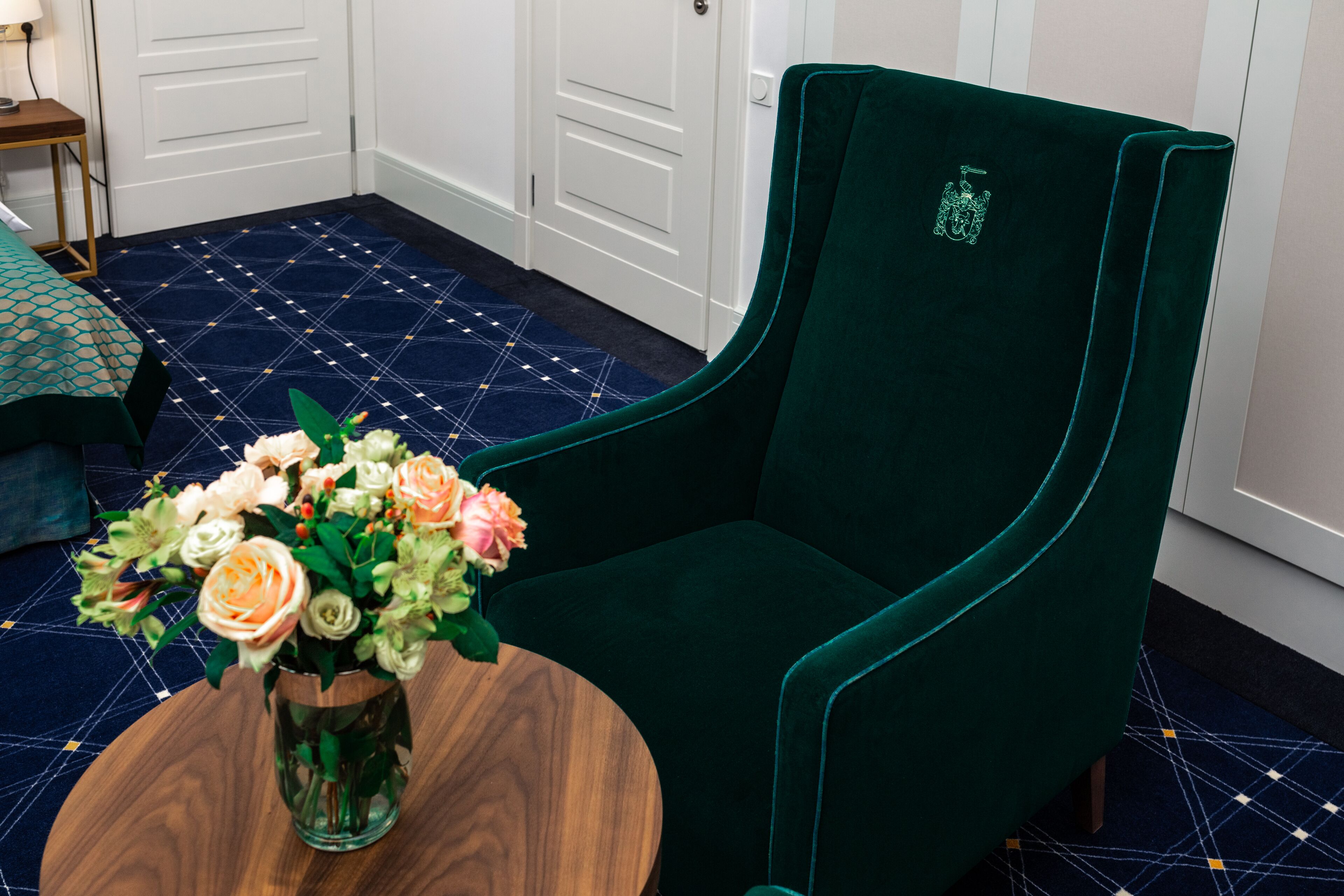 A green velvet armchair with a floral vase on a round wooden table.