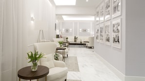 Una sala de estar moderna con un sofá blanco, una mesa redonda con un jarrón de flores y una mesa de centro. Hay cuadros enmarcados en la pared y una escalera al fondo.