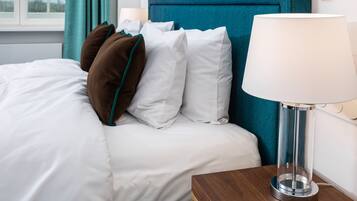 Una cama bien hecha con almohadas blancas y marrones, un cabecero color aguamarina y una mesita de noche con una lámpara.