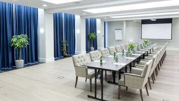 A conference room with a long table, chairs, potted plants, and a projector screen.