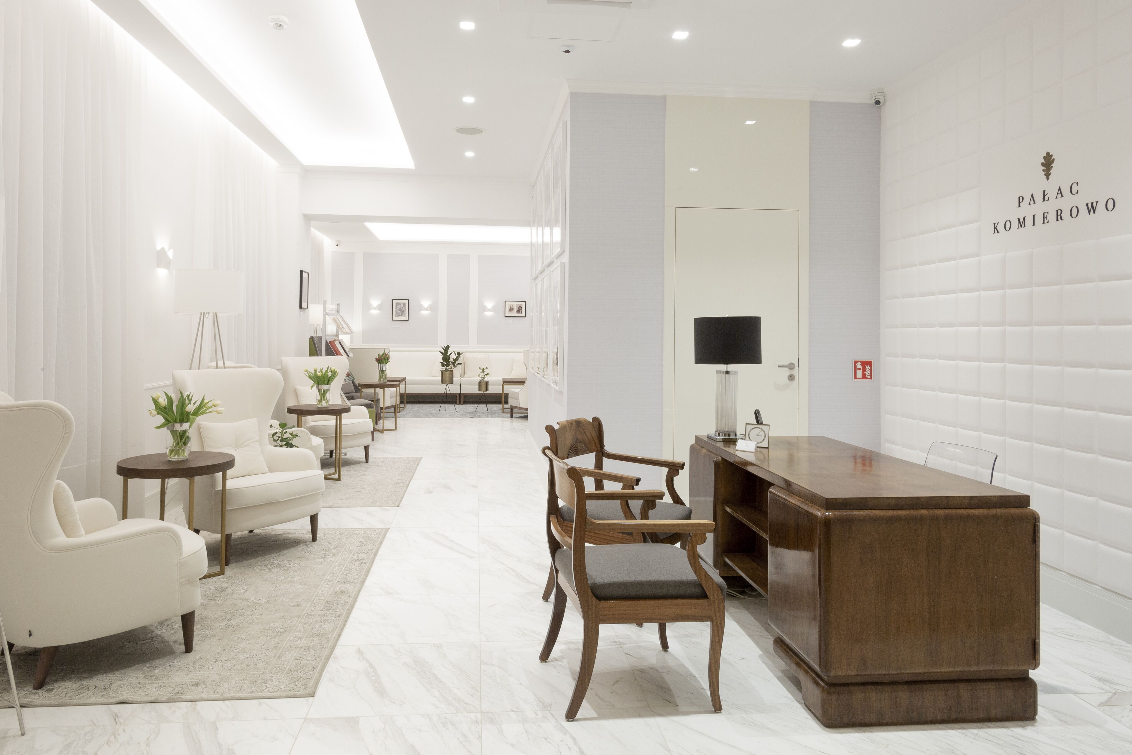 A modern hotel lobby with a reception desk, seating area, and a view into the dining area.