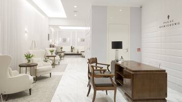 A modern hotel lobby with a reception desk, seating area, and a view into the dining area.