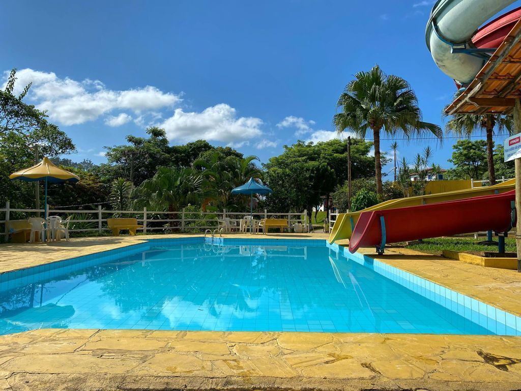 A swimming pool with a slide, surrounded by palm trees and a fenced area with outdoor seating.