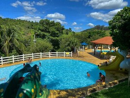 Piscina com toboáguas, rodeada por vegetação exuberante e um muro branco.