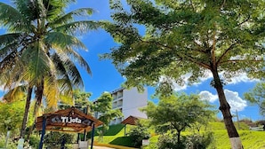 A tropical resort entrance with a wooden pavilion labeled "Ti jota," palm trees, and a building in the background. - Tijota Park Hotel Fazenda (Santana Do Paraiso)