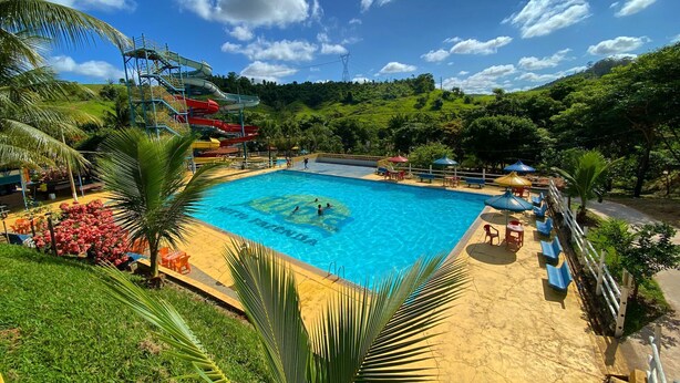 A swimming pool with a water slide, surrounded by palm trees and a hilly landscape. - Tijota Park Hotel Fazenda (Santana Do Paraiso)