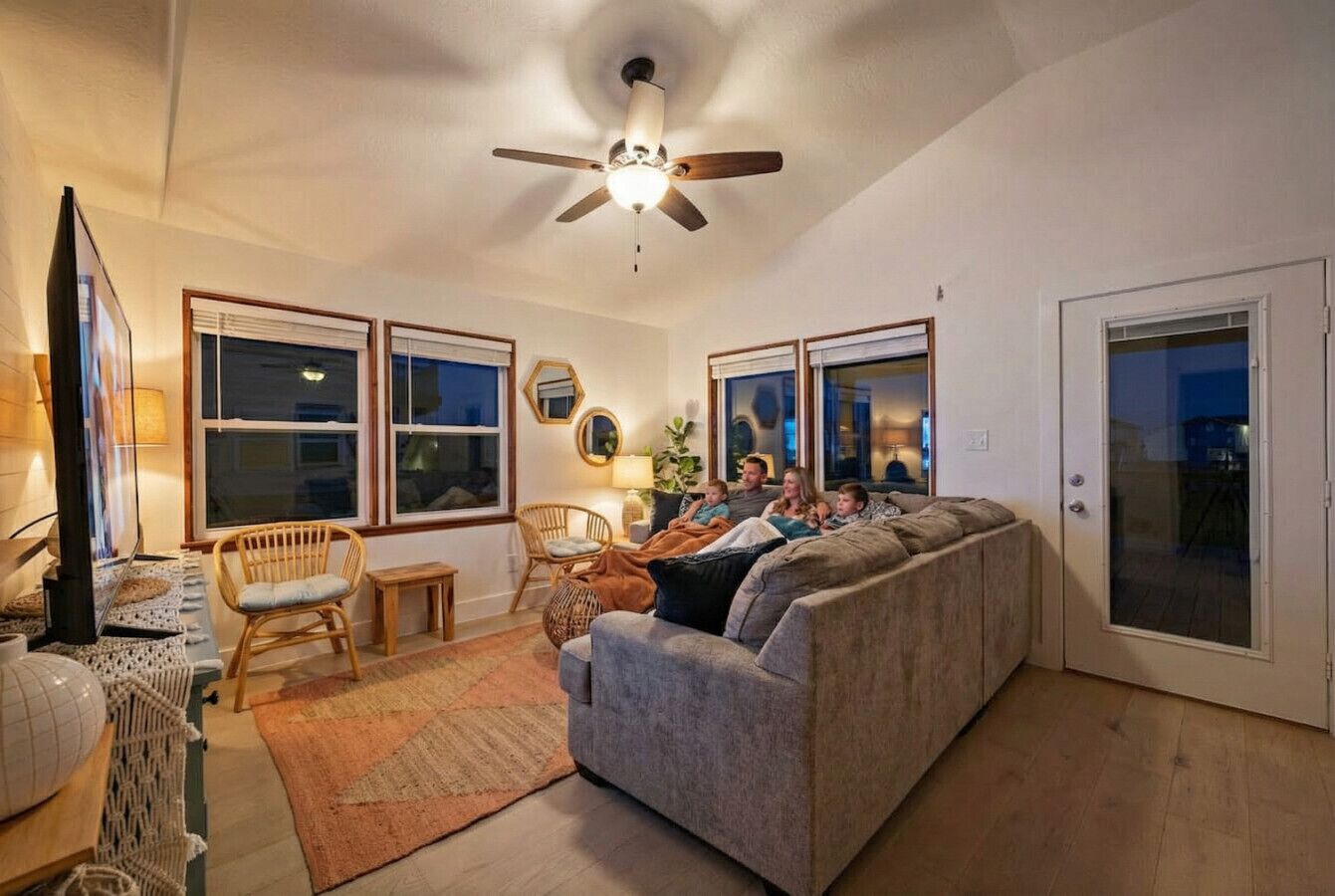 A cozy living room with a grey sofa, a ceiling fan, and a large window.