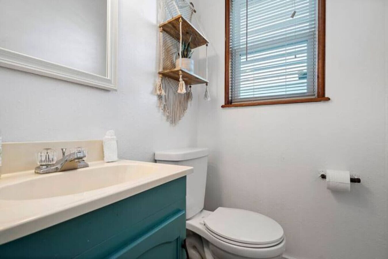Et badeværelse med en hvid vask, toilet og et vindue med persienner.