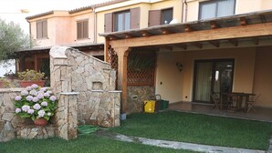 Una casa de dos pisos amb un mur de pedra i una zona de terrassa coberta.