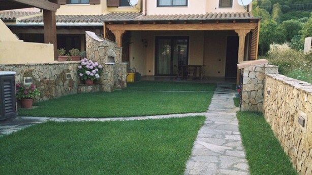 Una casa amb un camí de pedra que condueix a un pati, envoltat per una paret de pedra i un jardí ben cuidat.