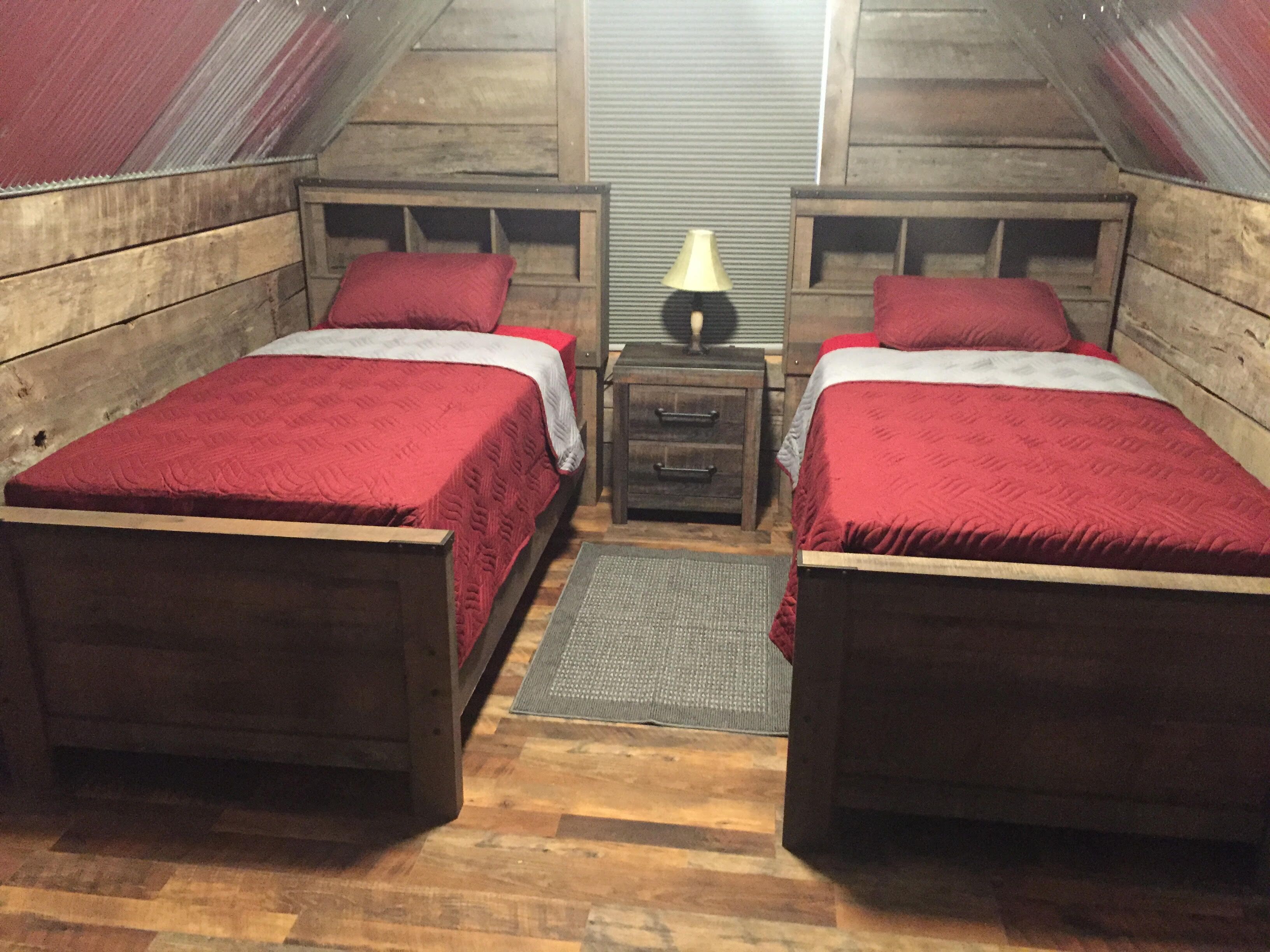 A small, cozy attic bedroom with two wooden beds, a nightstand, and a lamp.