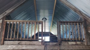 A wooden cabin with a loft bedroom, a metal roof, and a wooden staircase.
