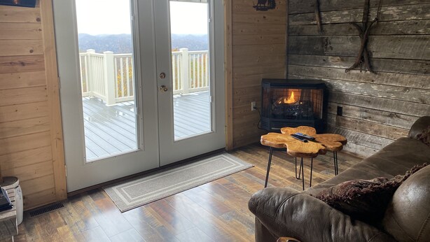A cozy cabin interior with a fireplace, wooden walls, and a deck with a view of mountains.