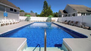 En swimmingpool med metalstige, liggestole og parasoller.