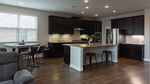 Una cocina moderna con armarios oscuros, una isla central y una zona de comedor con sillas.