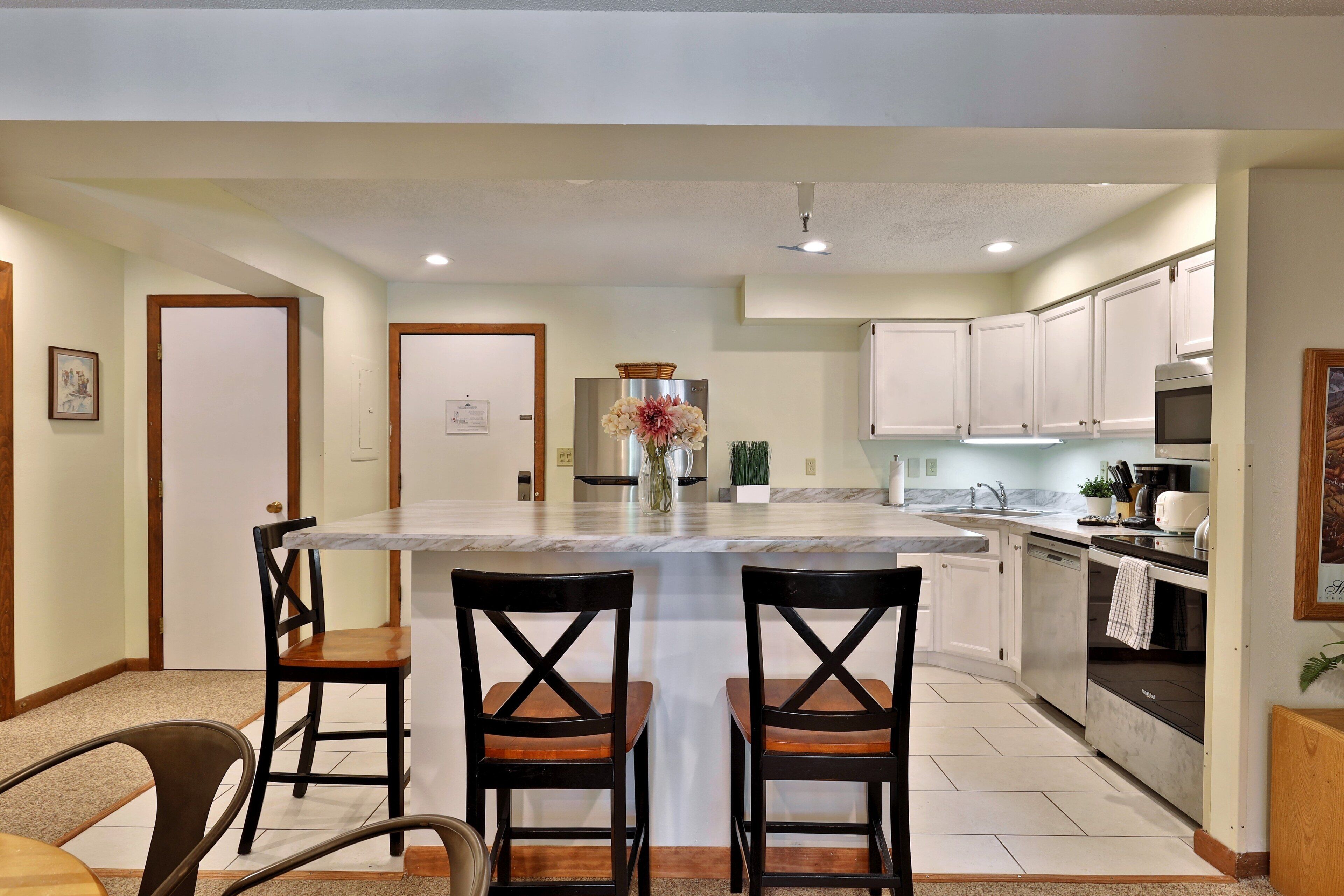 A modern kitchen with white cabinets, a marble island, and two wooden chairs.