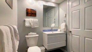 A bathroom with a toilet, sink, and mirror. There are towels hanging on the wall and a door to the right.
