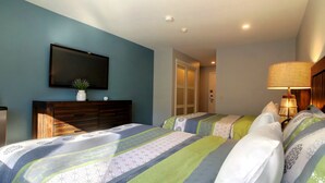 A hotel room with two beds, a TV on the wall, a bedside lamp, and a wardrobe.
