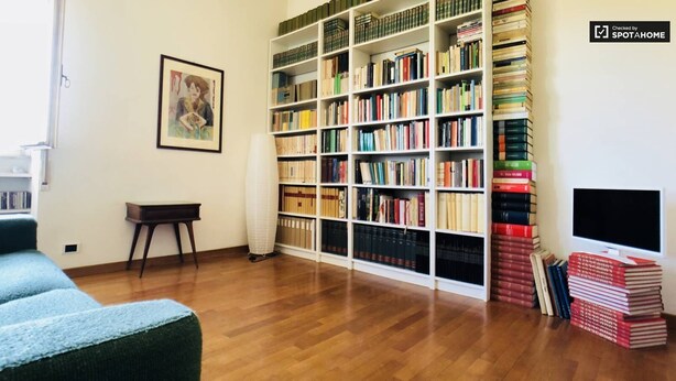 Ein Wohnzimmer mit Holzboden, einer Bücherwand, einem gerahmten Bild an der Wand und einem Fernseher auf einem Schrank.