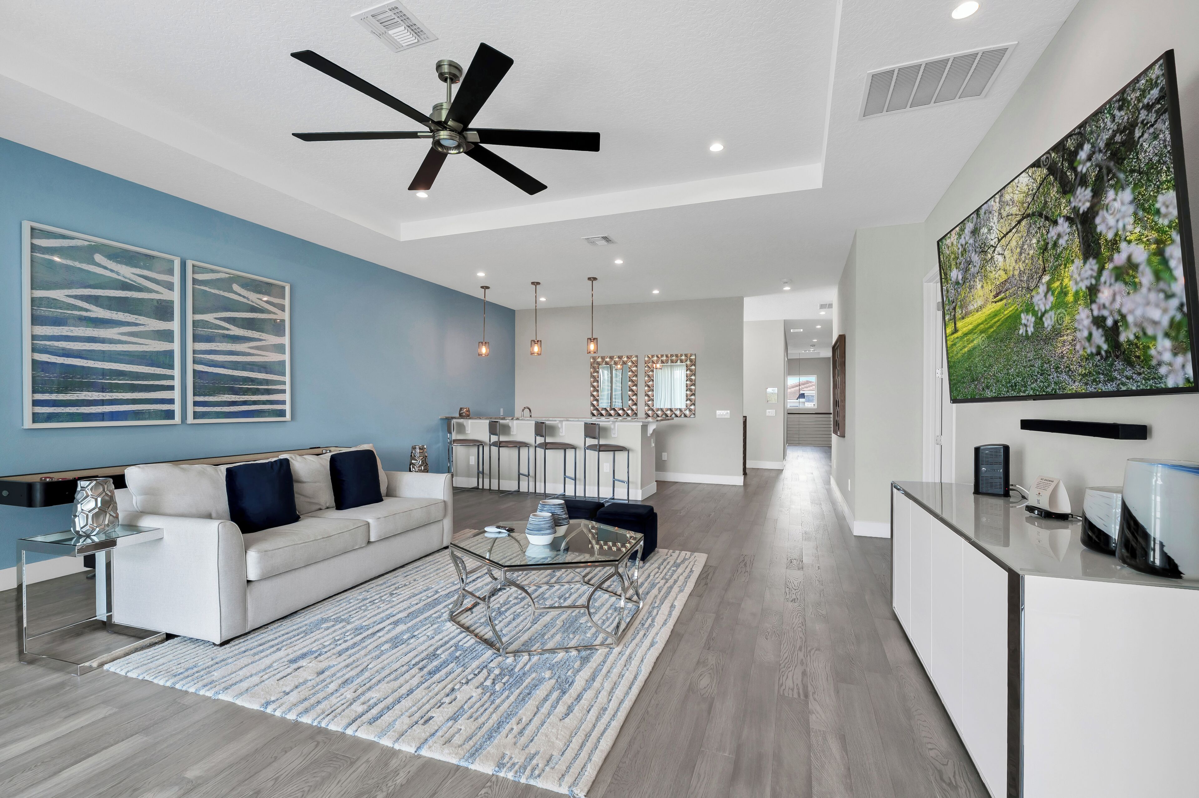 A modern living room with a white sofa, a glass coffee table, and a ceiling fan.