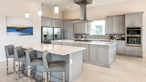 Una cocina moderna con gabinetes grises, electrodomésticos de acero inoxidable y una isla central con taburetes de bar.