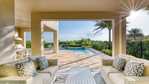 Un patio al aire libre con piscina, dos sofás con cojines estampados y una mesa blanca.