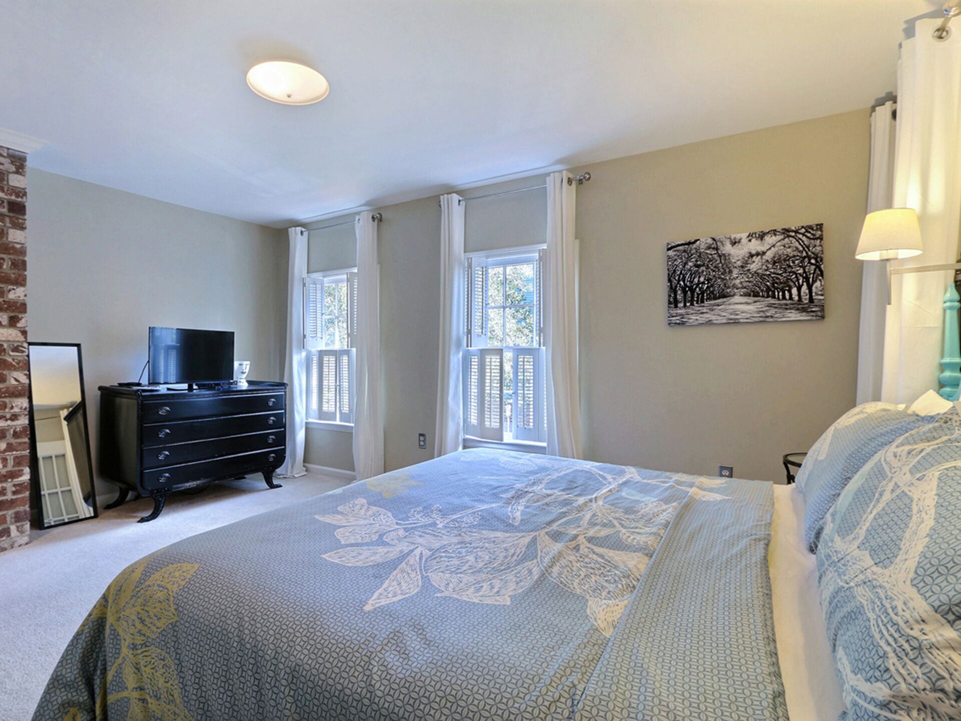 A bedroom with a bed, dresser, television, and windows.
