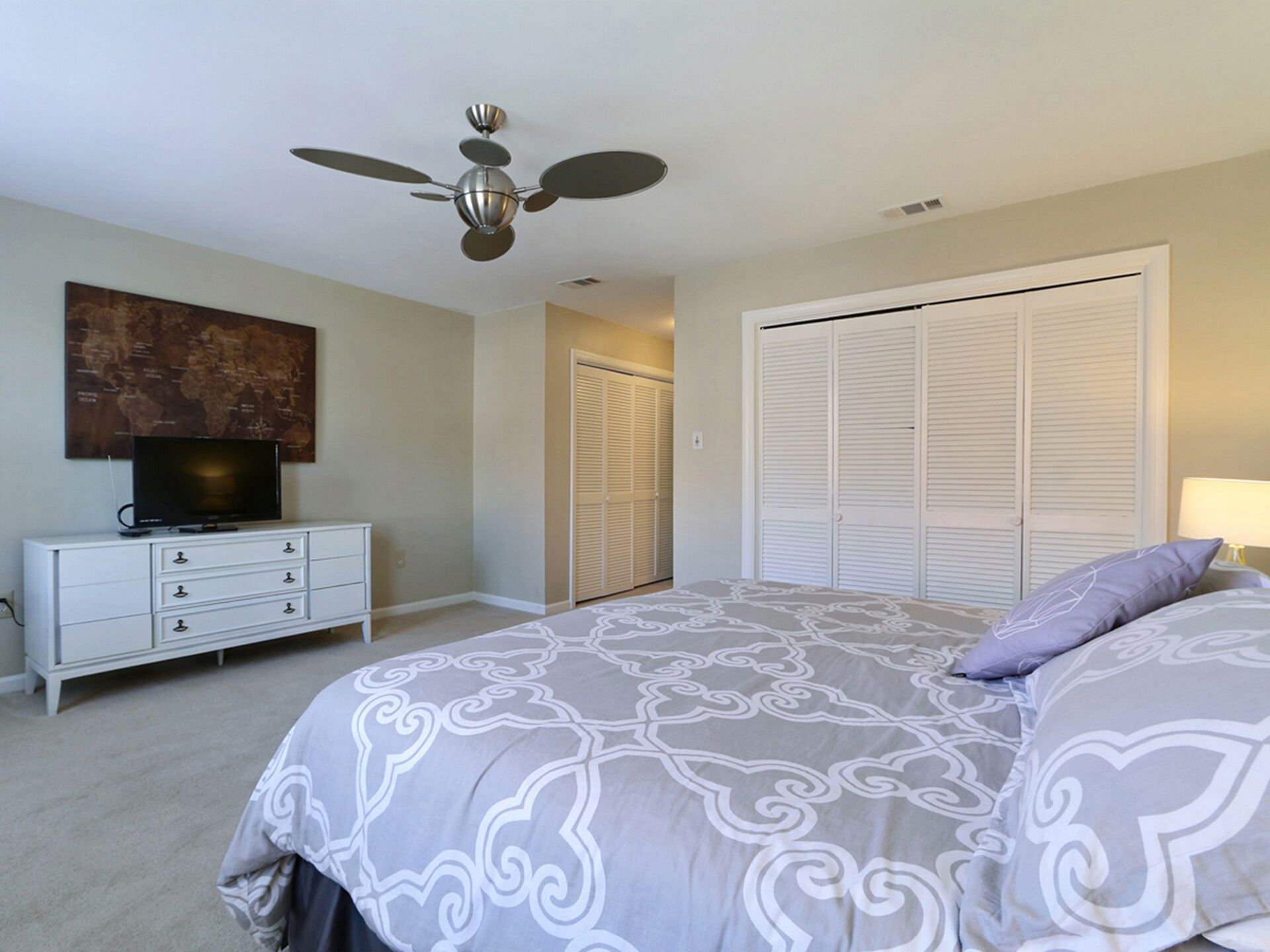 Une chambre à coucher avec un lit, un ventilateur de plafond, un téléviseur posé sur une commode et une armoire.