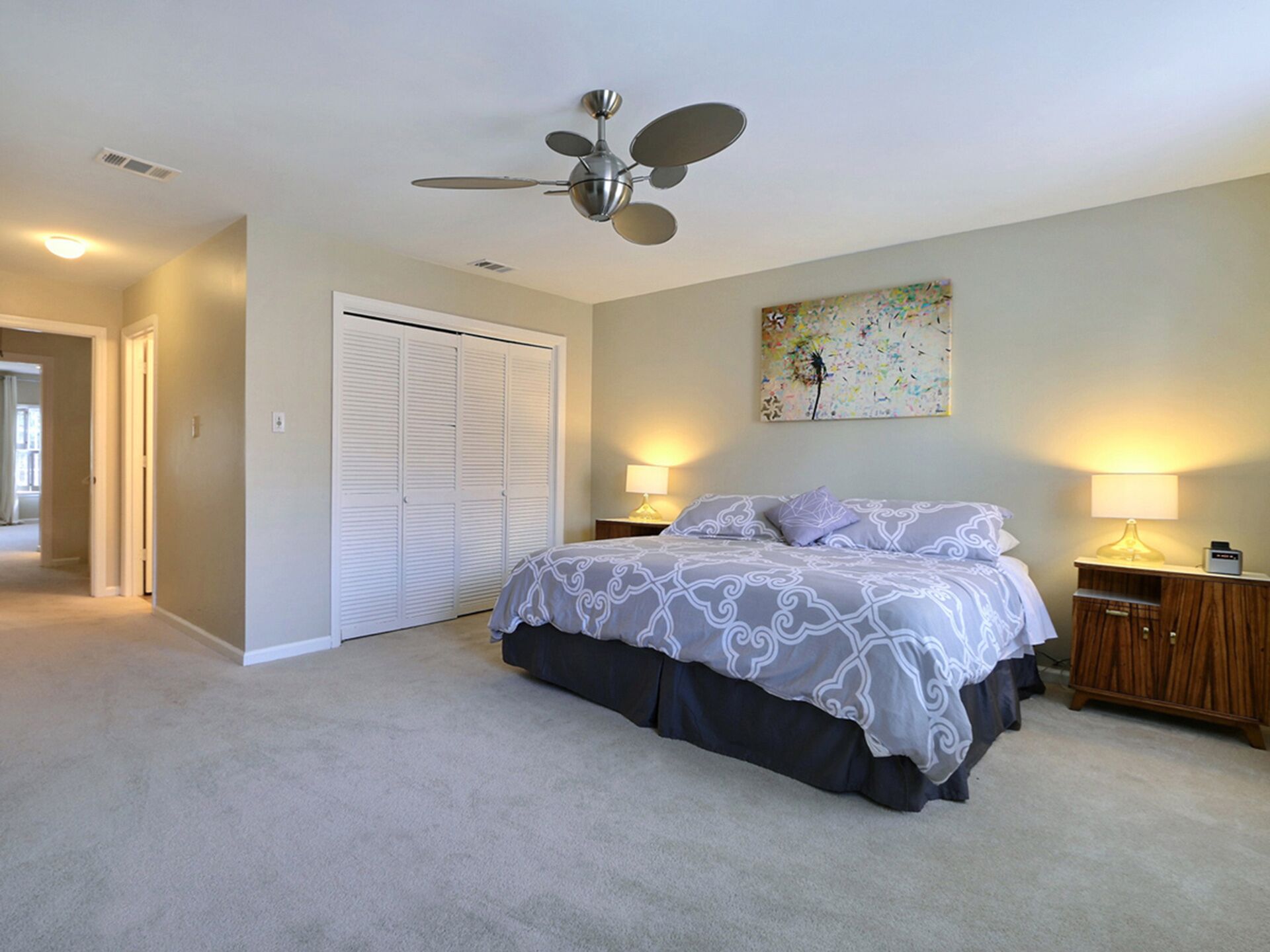 A bedroom with a bed, a ceiling fan, a closet, and a painting on the wall.
